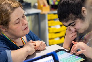 Student using an AAC communication device supported by a Teaching Assistant