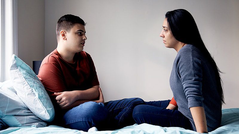 Mother and son sitting on a bed having a discussion